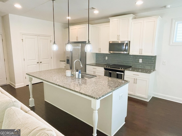 kitchen with stainless steel appliances, dark stone counters, sink, hanging light fixtures, and a center island with sink