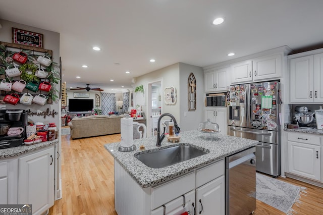 kitchen with white cabinets, stainless steel appliances, light hardwood / wood-style floors, sink, and a center island with sink