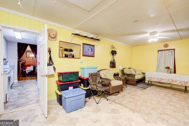 living area with ceiling fan and wooden walls