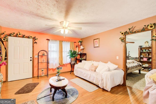 living room with ceiling fan, a textured ceiling, and light wood-type flooring