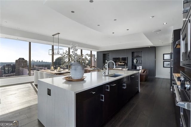 kitchen with dark hardwood / wood-style floors, pendant lighting, a raised ceiling, sink, and an island with sink