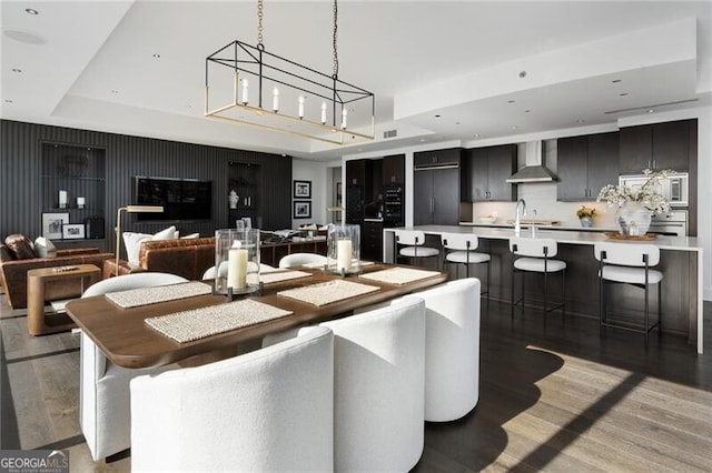 dining space featuring dark wood-type flooring, a raised ceiling, sink, and a chandelier