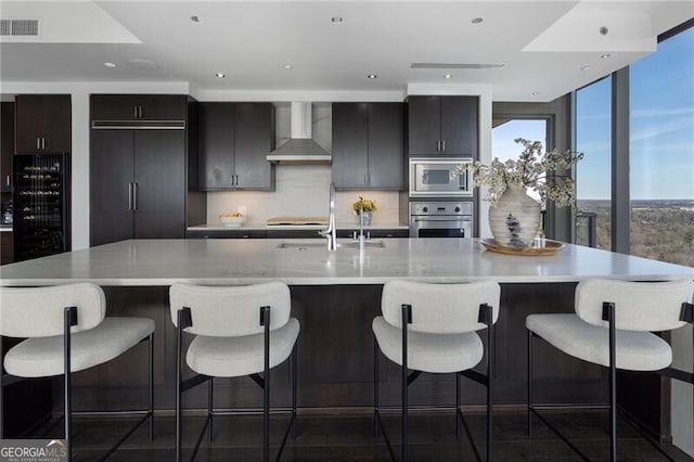 kitchen with a breakfast bar area, backsplash, built in appliances, and wall chimney range hood