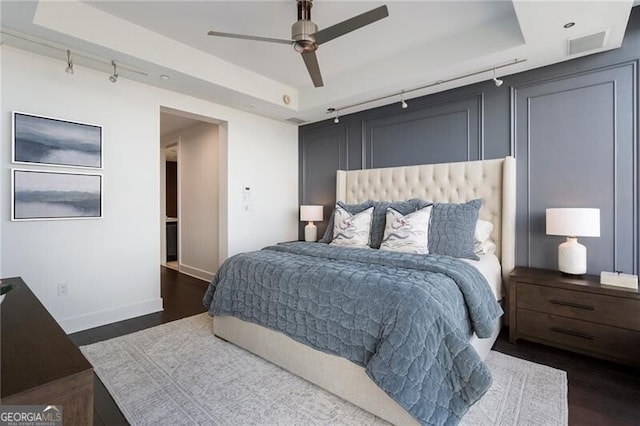 bedroom featuring ceiling fan, rail lighting, a raised ceiling, and dark wood-type flooring