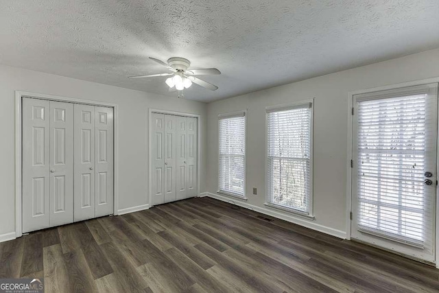 unfurnished bedroom with ceiling fan, dark wood-type flooring, a textured ceiling, and two closets