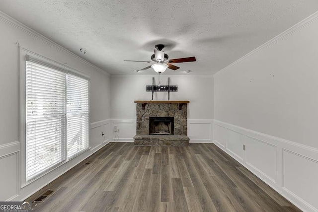 unfurnished living room with a stone fireplace, ceiling fan, dark hardwood / wood-style flooring, a textured ceiling, and ornamental molding