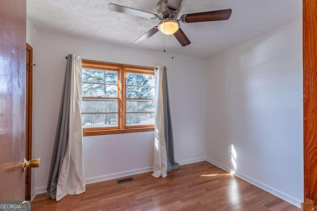 empty room with ceiling fan, light wood-type flooring, and a textured ceiling