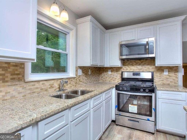 kitchen featuring appliances with stainless steel finishes, white cabinetry, decorative backsplash, sink, and hanging light fixtures