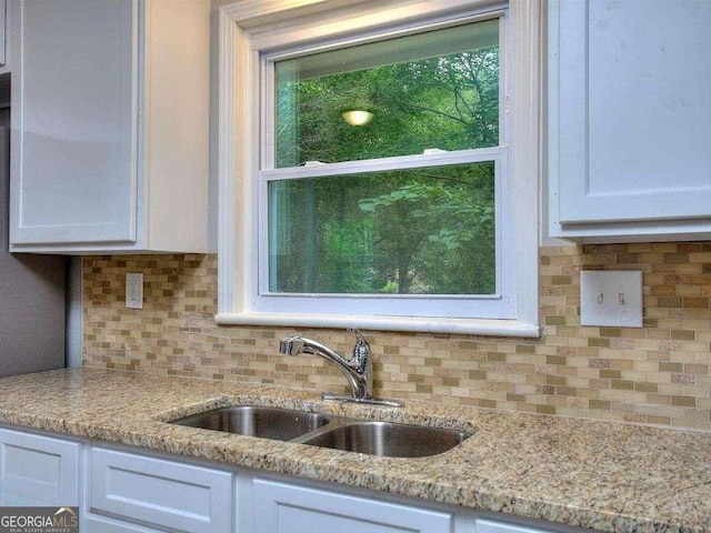 kitchen with backsplash, white cabinets, light stone counters, and sink