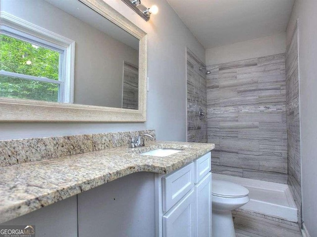 bathroom featuring toilet, vanity, and a tile shower