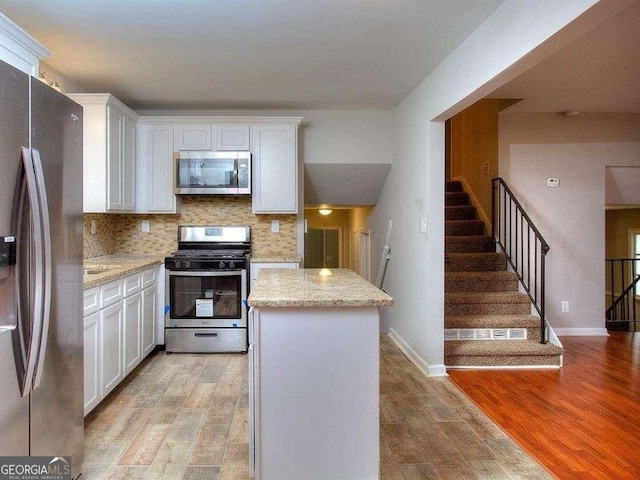 kitchen featuring light wood-type flooring, stainless steel appliances, white cabinetry, and light stone countertops