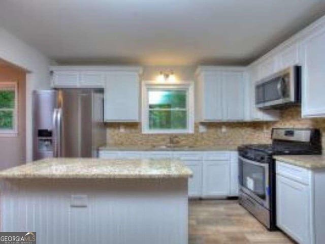 kitchen featuring light stone countertops, appliances with stainless steel finishes, white cabinetry, and a center island