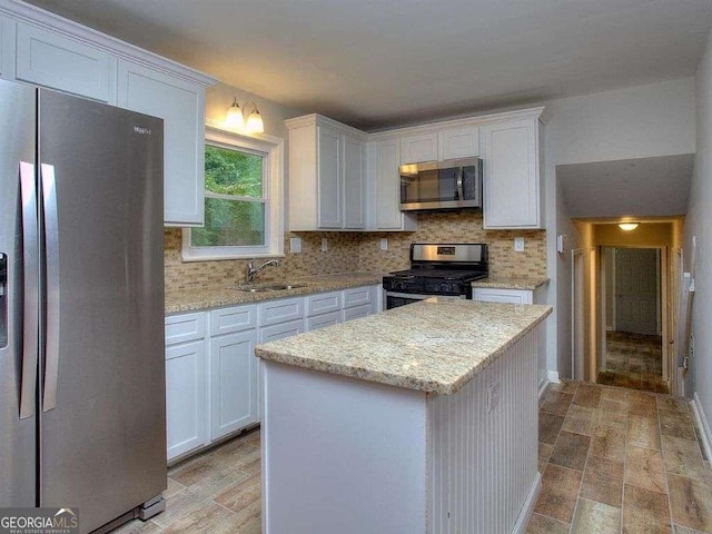 kitchen featuring light stone countertops, white cabinets, appliances with stainless steel finishes, a kitchen island, and sink