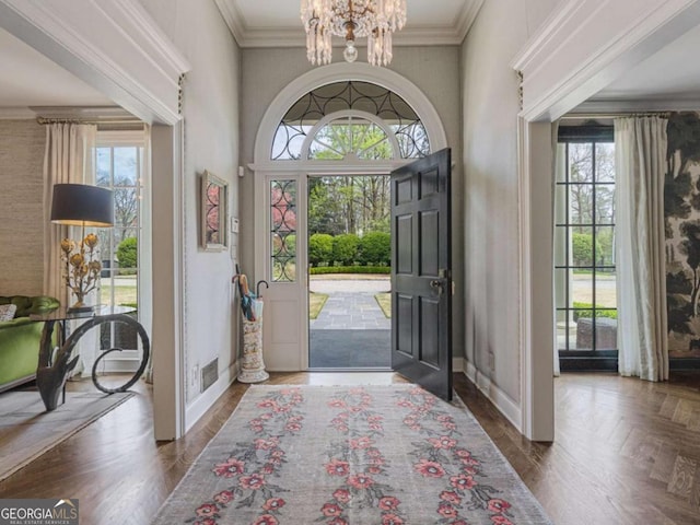 foyer with an inviting chandelier, baseboards, visible vents, and ornamental molding