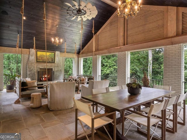 dining room with wood ceiling, stone tile flooring, a fireplace, high vaulted ceiling, and a notable chandelier