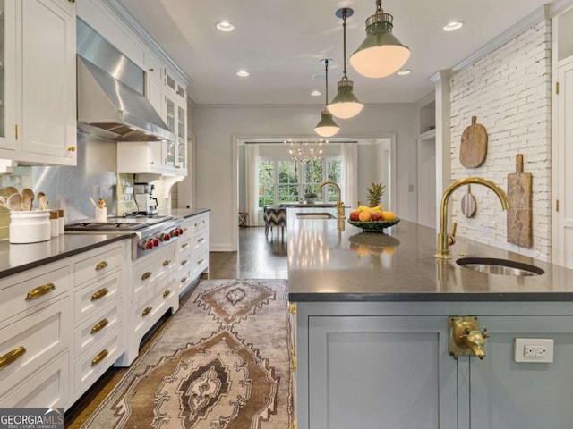 kitchen with decorative backsplash, white cabinetry, a sink, and wall chimney exhaust hood