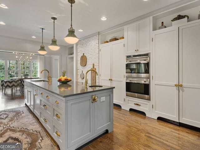 kitchen with stainless steel double oven, dark wood-style flooring, a center island with sink, and a sink