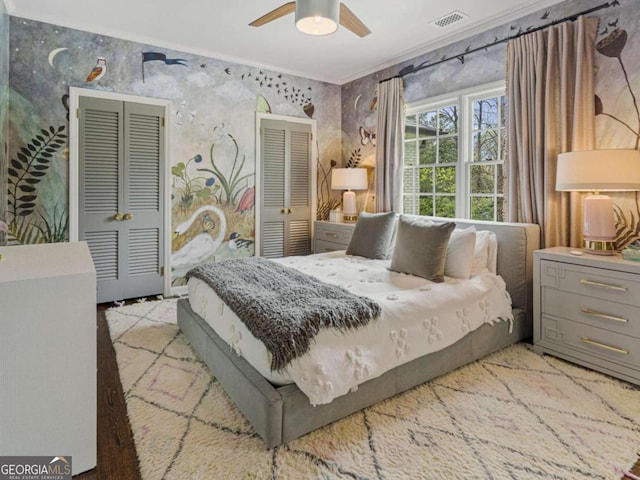 bedroom with a ceiling fan, visible vents, crown molding, and two closets