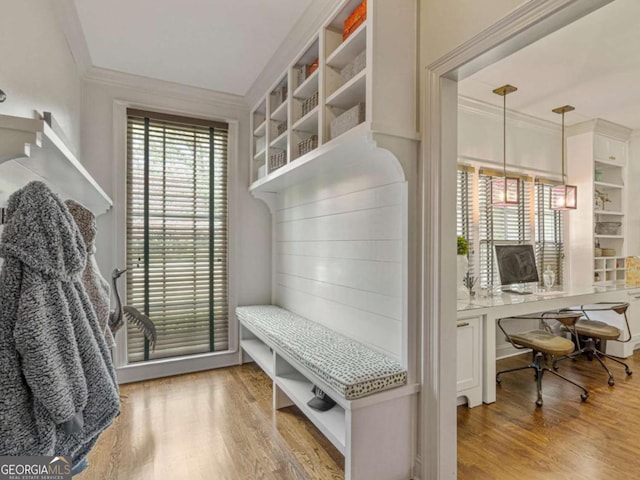 mudroom with built in desk, crown molding, and wood finished floors