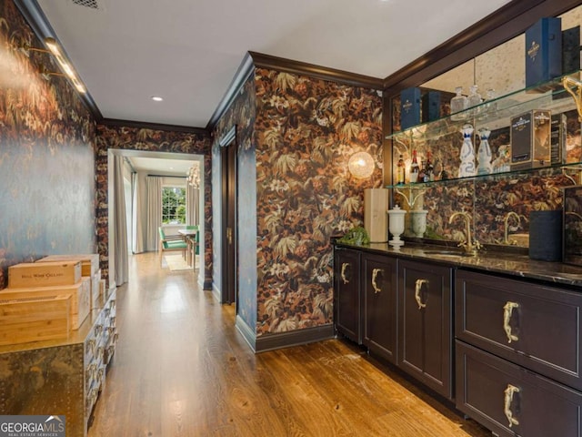 bar with wood finished floors, a sink, ornamental molding, indoor wet bar, and wallpapered walls