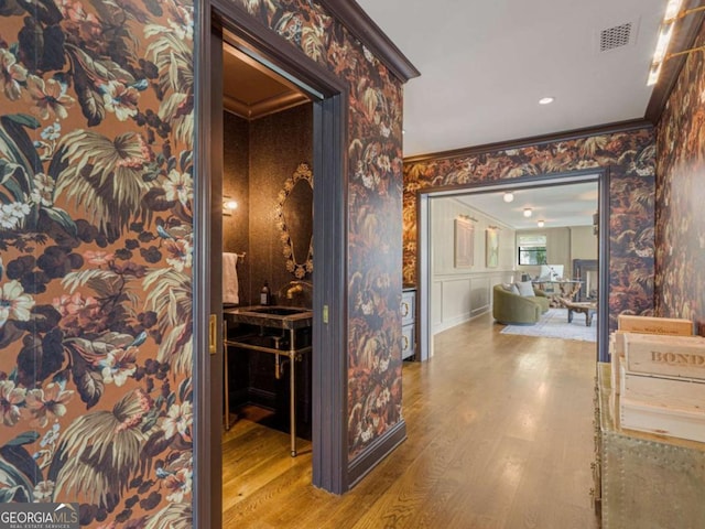 hallway with a sink, wood finished floors, visible vents, ornamental molding, and wallpapered walls