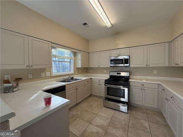 kitchen featuring kitchen peninsula, sink, light tile patterned floors, appliances with stainless steel finishes, and white cabinets