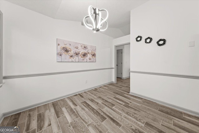 empty room with wood-type flooring, an inviting chandelier, and vaulted ceiling