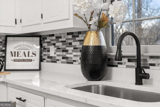 interior details with tasteful backsplash, light stone countertops, sink, and white cabinetry