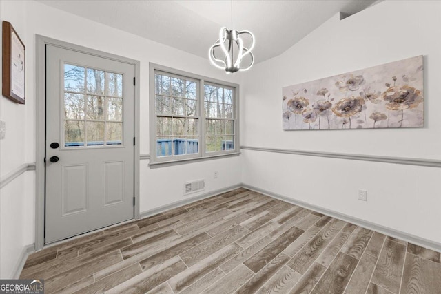 unfurnished dining area with a chandelier, lofted ceiling, and wood-type flooring