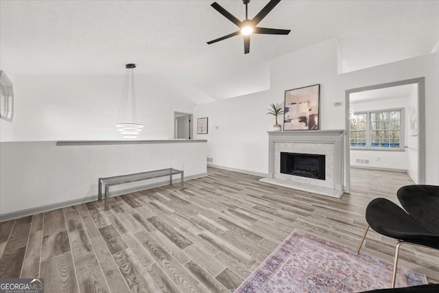 living room featuring light hardwood / wood-style floors, a high end fireplace, lofted ceiling, and ceiling fan