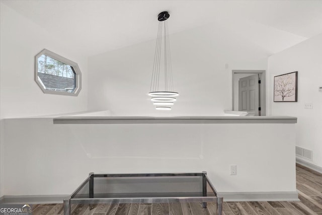 interior space with kitchen peninsula, hanging light fixtures, lofted ceiling, and hardwood / wood-style floors