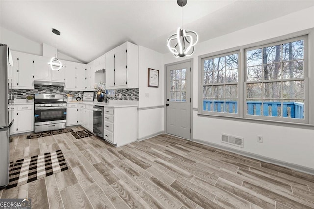 kitchen featuring stainless steel range with gas stovetop, backsplash, decorative light fixtures, lofted ceiling, and white cabinets