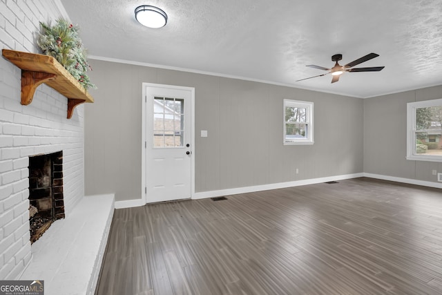 unfurnished living room with a textured ceiling, dark wood-type flooring, crown molding, and a fireplace