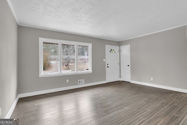 empty room featuring dark wood-type flooring, a textured ceiling, and crown molding