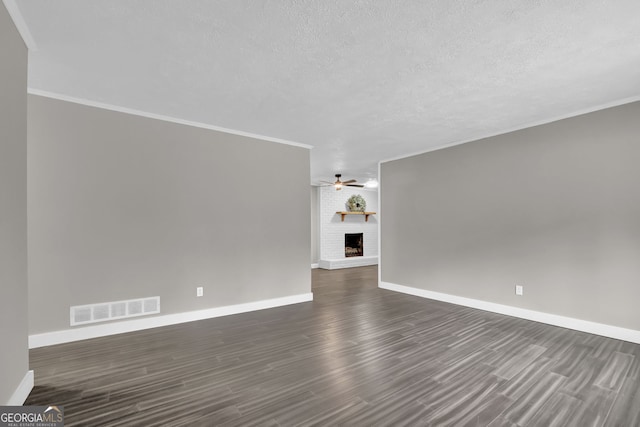 spare room with ceiling fan, a fireplace, dark hardwood / wood-style floors, crown molding, and a textured ceiling