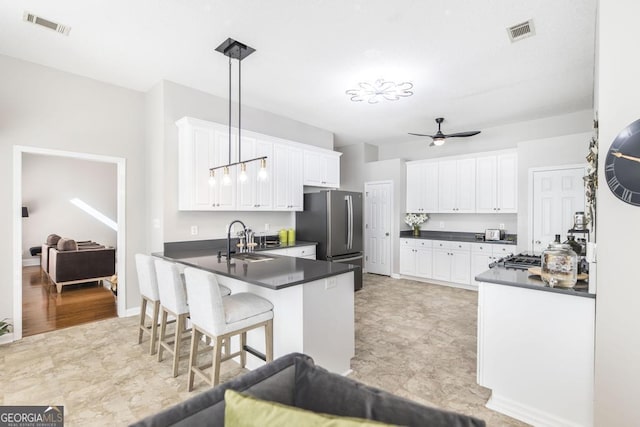 kitchen featuring pendant lighting, white cabinets, a kitchen bar, sink, and stainless steel refrigerator