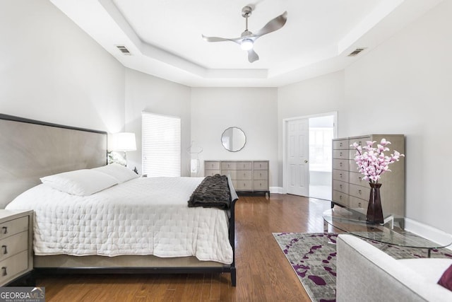 bedroom with ceiling fan, dark hardwood / wood-style flooring, and a tray ceiling