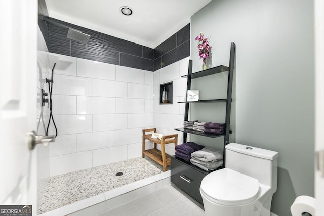 bathroom with toilet, a tile shower, and tile patterned floors