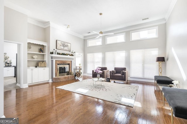 living room featuring a high ceiling, dark wood-type flooring, built in shelves, a fireplace, and ceiling fan