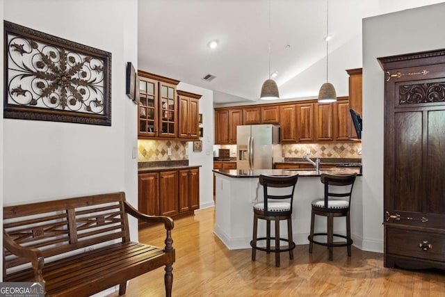 kitchen featuring decorative light fixtures, stainless steel refrigerator with ice dispenser, decorative backsplash, light wood-type flooring, and a kitchen island with sink