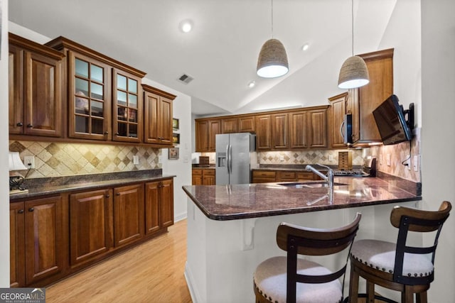 kitchen featuring stainless steel appliances, backsplash, decorative light fixtures, light wood-type flooring, and lofted ceiling