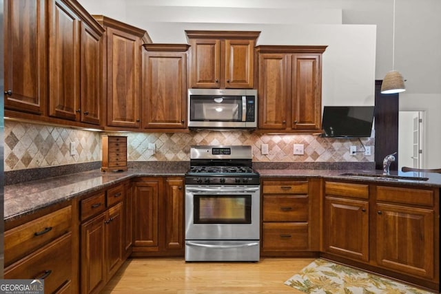 kitchen with appliances with stainless steel finishes, dark stone counters, sink, backsplash, and hanging light fixtures