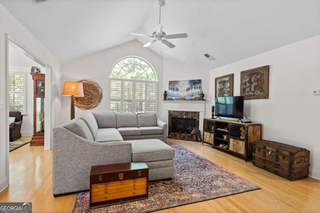 living room with light wood-type flooring, ceiling fan, vaulted ceiling, and a fireplace