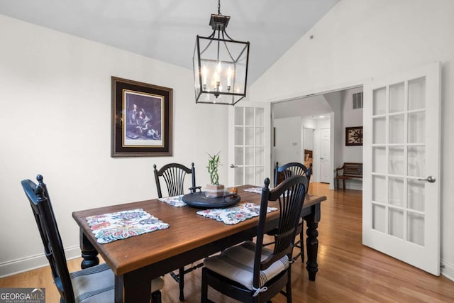 dining space featuring hardwood / wood-style floors, lofted ceiling, french doors, and a notable chandelier