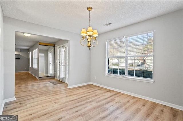 unfurnished dining area with a textured ceiling, light hardwood / wood-style flooring, and an inviting chandelier