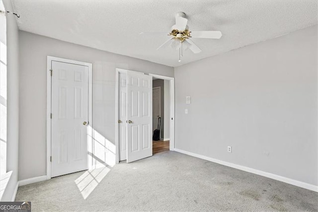 unfurnished bedroom with light carpet, ceiling fan, and a textured ceiling