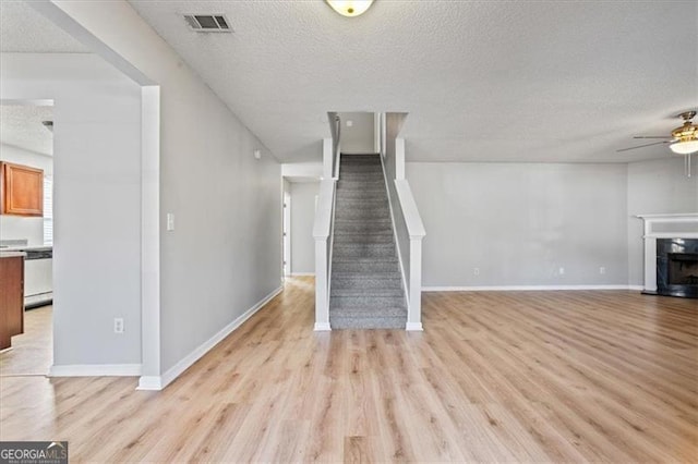 unfurnished living room featuring ceiling fan, a textured ceiling, a premium fireplace, and light wood-type flooring