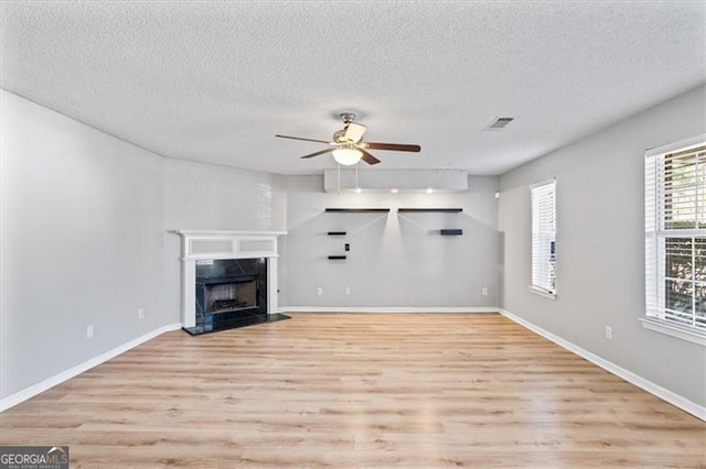 unfurnished living room featuring a textured ceiling, a premium fireplace, light hardwood / wood-style floors, and ceiling fan