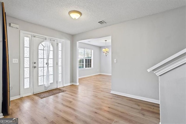 foyer entrance with light wood-type flooring, a textured ceiling, and a notable chandelier