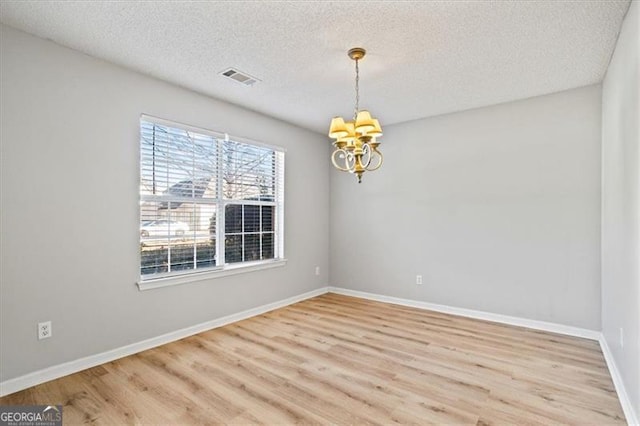 unfurnished room featuring a textured ceiling, a chandelier, and hardwood / wood-style flooring